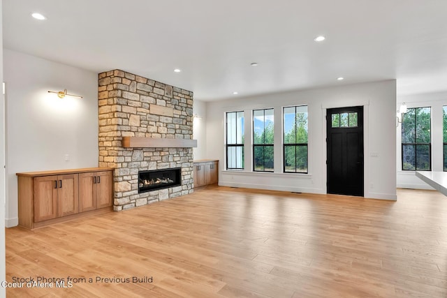 unfurnished living room with a stone fireplace, a wealth of natural light, and light hardwood / wood-style flooring