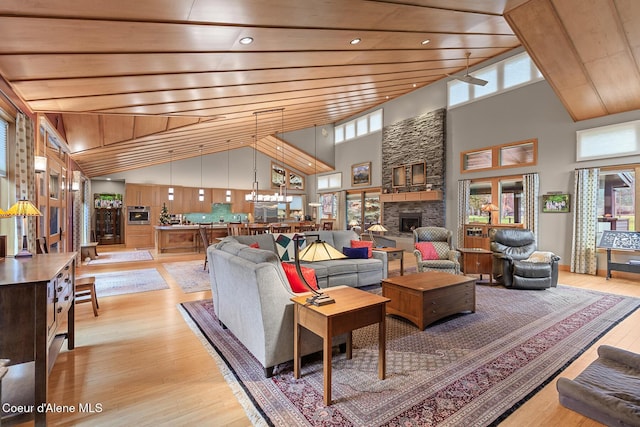 living room featuring a stone fireplace, high vaulted ceiling, and light hardwood / wood-style floors