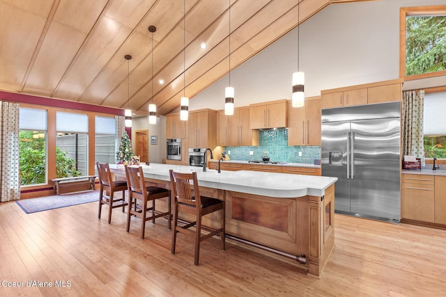 kitchen featuring backsplash, stainless steel appliances, a kitchen island with sink, pendant lighting, and high vaulted ceiling