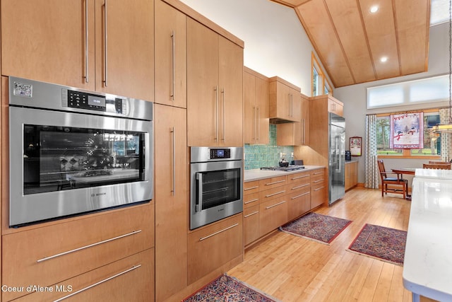 kitchen featuring high vaulted ceiling, decorative backsplash, light brown cabinetry, appliances with stainless steel finishes, and light hardwood / wood-style floors