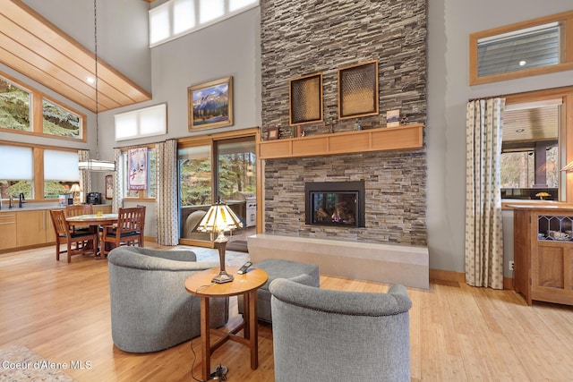 living room with a stone fireplace, a towering ceiling, and light hardwood / wood-style floors