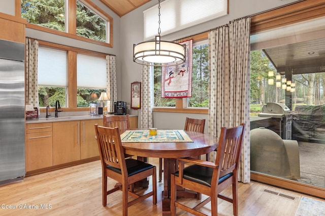 dining area featuring light wood-type flooring, sink, and high vaulted ceiling