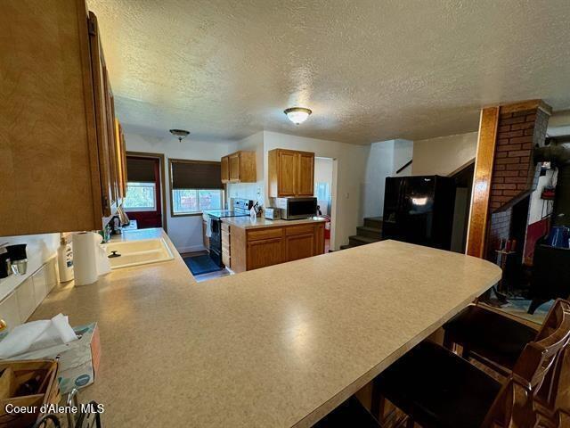 kitchen featuring kitchen peninsula, a breakfast bar, a textured ceiling, sink, and black appliances