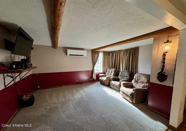 home theater with beamed ceiling, dark carpet, an AC wall unit, and a textured ceiling