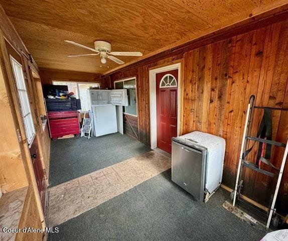 interior space featuring ceiling fan, dark carpet, wooden ceiling, and wooden walls