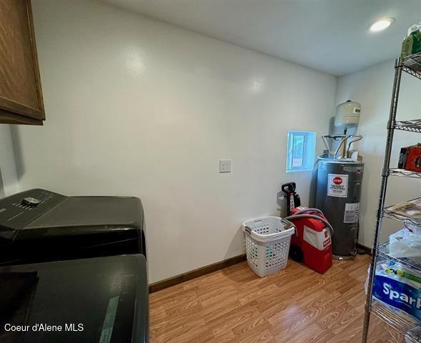 washroom with washing machine and dryer, electric water heater, light hardwood / wood-style flooring, and cabinets