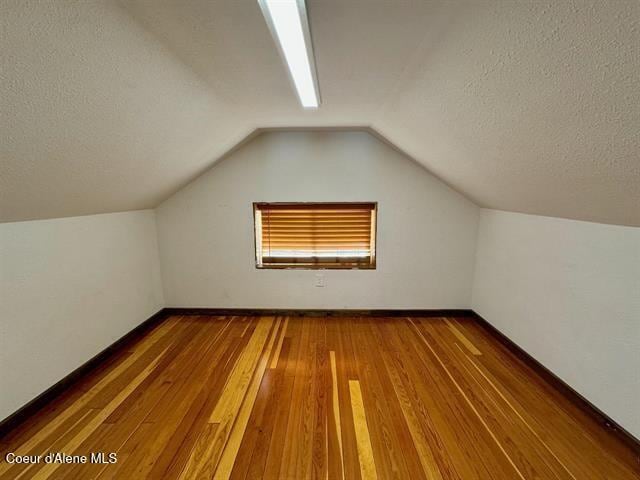 additional living space featuring a textured ceiling, dark wood-type flooring, and lofted ceiling