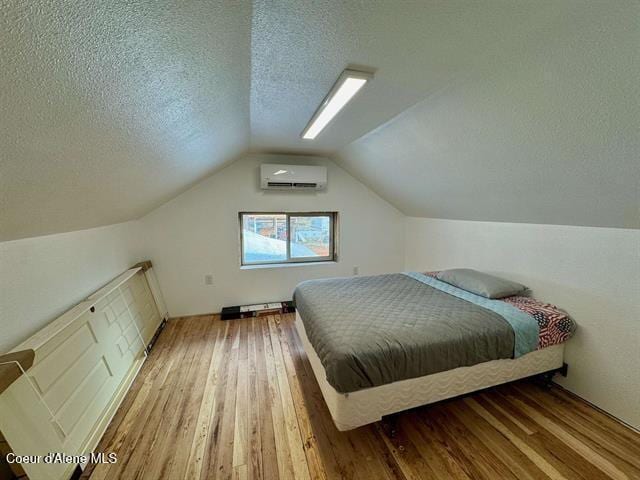 bedroom featuring wood-type flooring, a textured ceiling, a wall mounted AC, and lofted ceiling