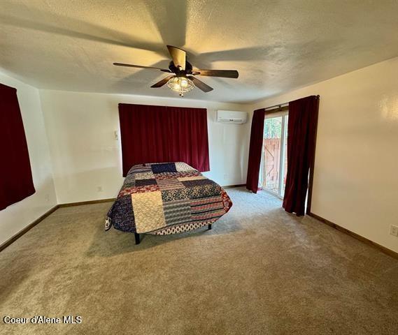 bedroom with a wall mounted air conditioner, a textured ceiling, carpet floors, and ceiling fan