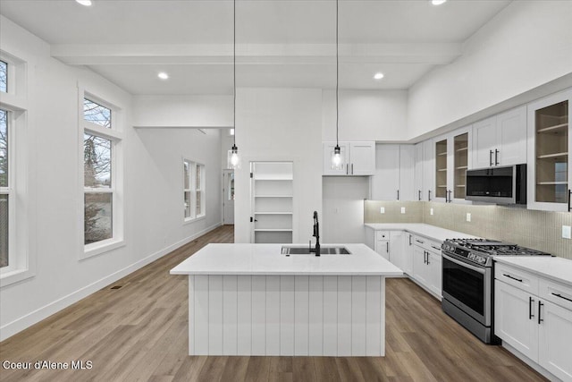 kitchen featuring beam ceiling, sink, stainless steel appliances, pendant lighting, and a kitchen island with sink