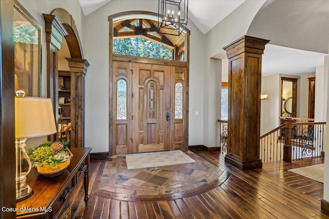 foyer featuring dark hardwood / wood-style floors, ornate columns, lofted ceiling, and a notable chandelier