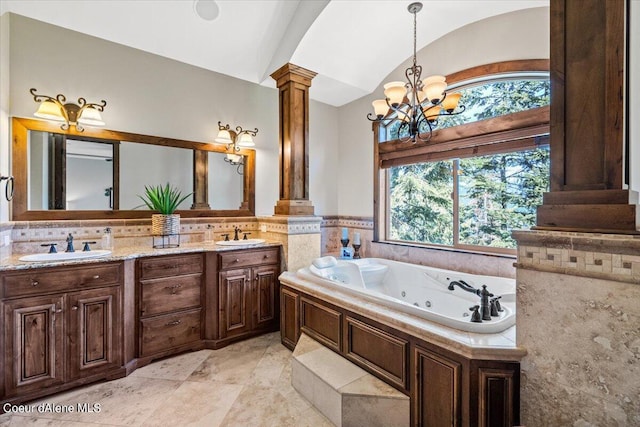 bathroom featuring decorative columns, vanity, vaulted ceiling, tiled tub, and a notable chandelier