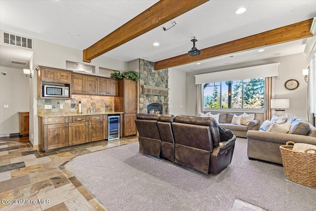 living room featuring beam ceiling, a fireplace, and beverage cooler