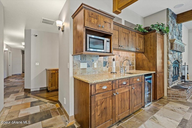 kitchen featuring stainless steel microwave, backsplash, sink, light stone counters, and beverage cooler