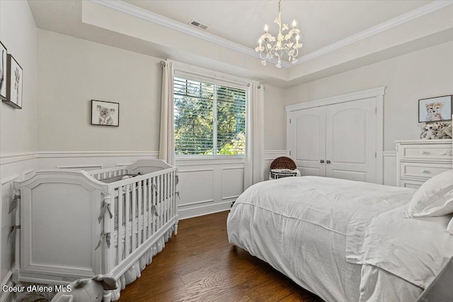 bedroom with ornamental molding, a tray ceiling, dark wood-type flooring, a chandelier, and a closet