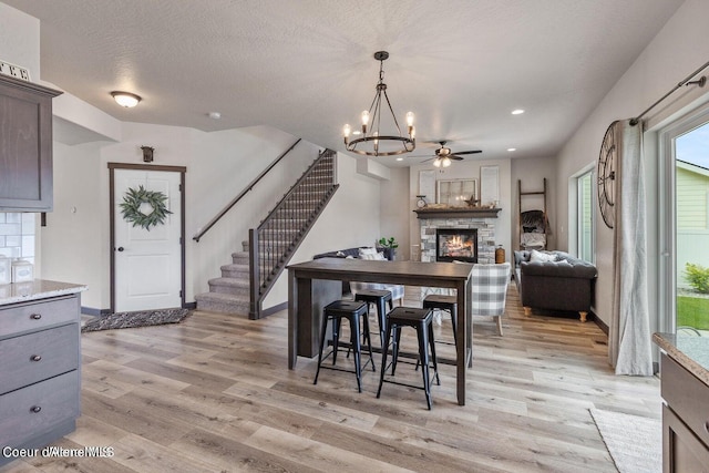 dining room featuring a textured ceiling, ceiling fan with notable chandelier, light wood-type flooring, and a fireplace