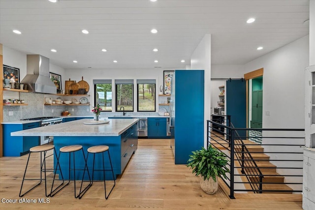 kitchen featuring high end stainless steel range oven, wall chimney range hood, blue cabinetry, light hardwood / wood-style floors, and a kitchen island