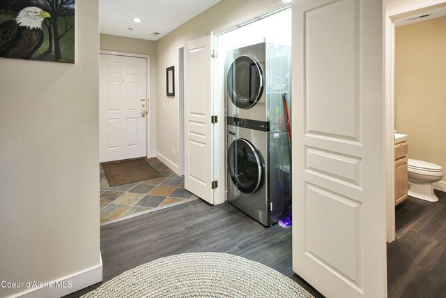 clothes washing area featuring stacked washing maching and dryer, baseboards, laundry area, and dark wood-style floors