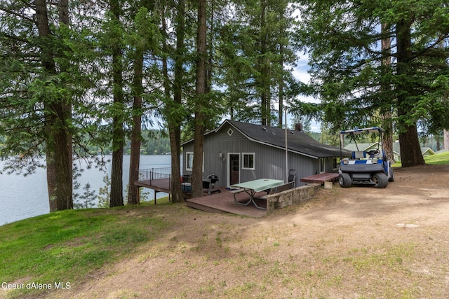 rear view of house with a deck with water view and a lawn