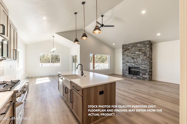 kitchen featuring ceiling fan, sink, light hardwood / wood-style flooring, a fireplace, and a center island with sink