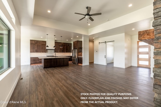 unfurnished living room with a barn door, ceiling fan, dark wood-type flooring, and sink