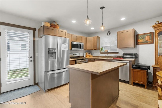 kitchen featuring sink, hanging light fixtures, stainless steel appliances, light hardwood / wood-style floors, and a kitchen island