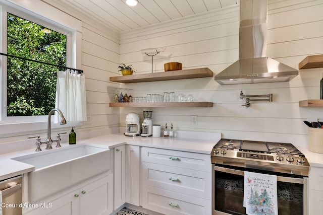 kitchen with appliances with stainless steel finishes, wooden walls, white cabinetry, and range hood