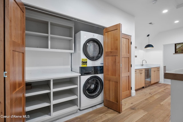 washroom with sink, beverage cooler, stacked washing maching and dryer, and light wood-type flooring