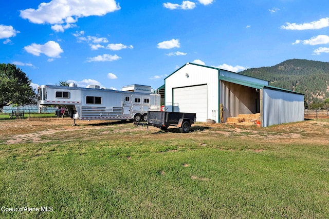 rear view of property featuring a mountain view, an outbuilding, a garage, and a lawn