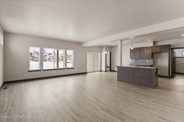 kitchen featuring backsplash, light stone counters, pendant lighting, a center island with sink, and light hardwood / wood-style floors