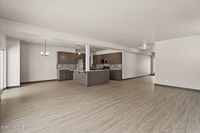 kitchen with hardwood / wood-style floors, a center island with sink, tasteful backsplash, decorative light fixtures, and a chandelier