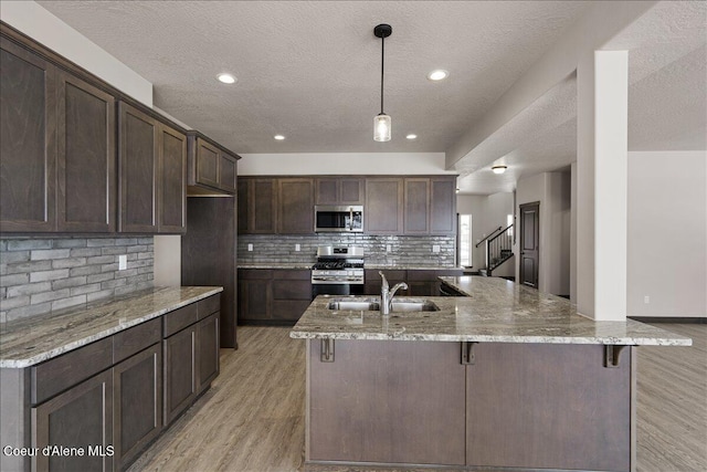 kitchen with light stone counters, dark brown cabinetry, stainless steel appliances, sink, and a breakfast bar area