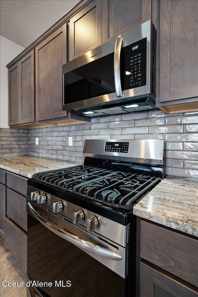 kitchen with dark brown cabinetry, light stone countertops, stainless steel appliances, and tasteful backsplash