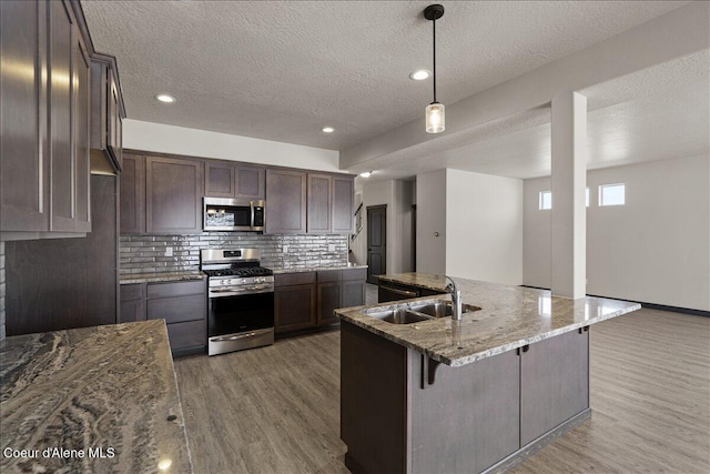 kitchen with dark brown cabinetry, sink, a textured ceiling, stone countertops, and appliances with stainless steel finishes