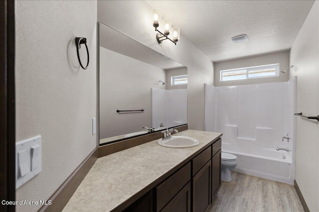 full bathroom with washtub / shower combination, a textured ceiling, toilet, vanity, and hardwood / wood-style flooring