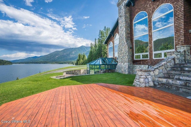 wooden deck featuring glass enclosure, a water and mountain view, and a lawn