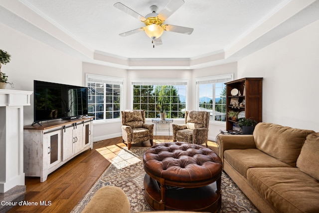 living room with a tray ceiling, ceiling fan, crown molding, and dark wood-type flooring