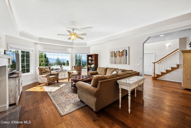 living room featuring dark hardwood / wood-style flooring, a tray ceiling, ceiling fan, and ornamental molding