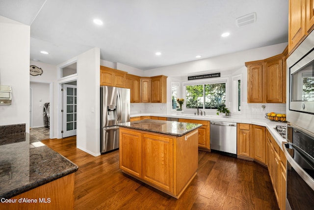 kitchen with a center island, dark wood-type flooring, dark stone counters, decorative backsplash, and appliances with stainless steel finishes