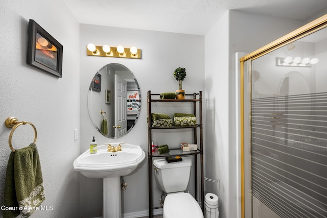 bathroom with a textured ceiling, toilet, a shower with shower door, and sink