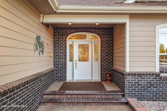 view of exterior entry featuring brick siding and roof with shingles