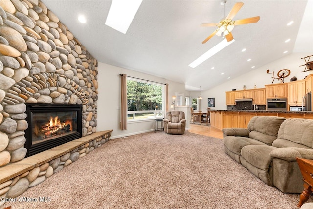 living area with a skylight, light carpet, ceiling fan, a stone fireplace, and a textured ceiling