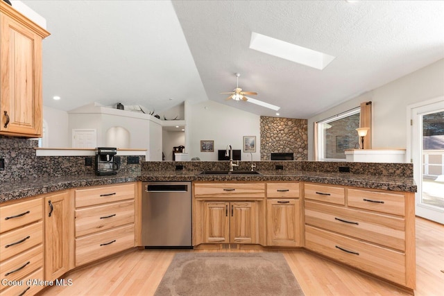 kitchen with light wood-style flooring, light brown cabinetry, lofted ceiling with skylight, a sink, and dishwasher