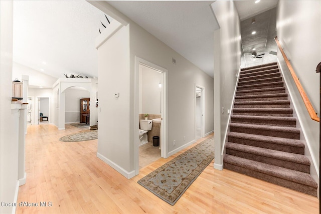 stairway with baseboards, visible vents, arched walkways, lofted ceiling, and wood finished floors