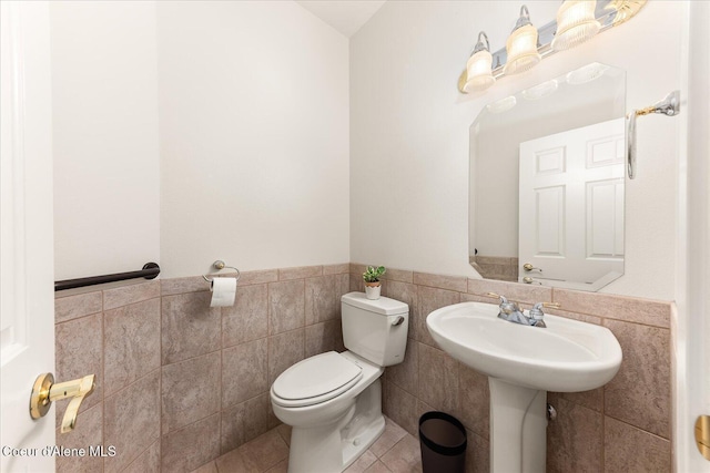 half bath featuring toilet, a wainscoted wall, tile walls, and tile patterned floors