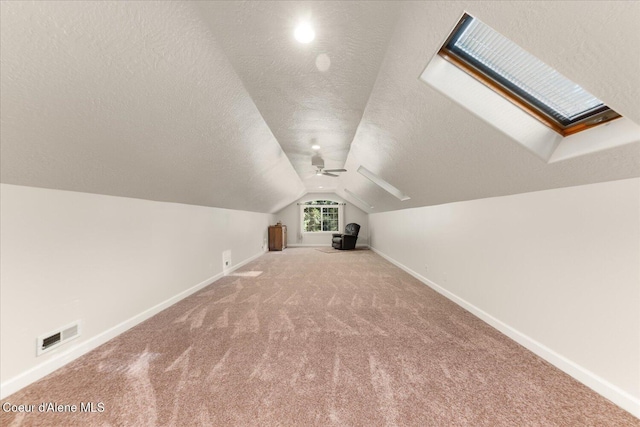 bonus room featuring baseboards, visible vents, lofted ceiling with skylight, a textured ceiling, and carpet floors