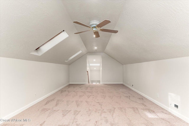 additional living space with vaulted ceiling with skylight, visible vents, a textured ceiling, and light colored carpet