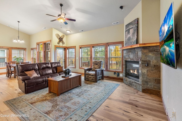 living room with ceiling fan with notable chandelier, light hardwood / wood-style floors, a stone fireplace, and a healthy amount of sunlight