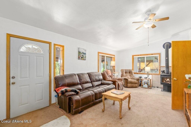 carpeted living room with ceiling fan, vaulted ceiling, a healthy amount of sunlight, and a wood stove