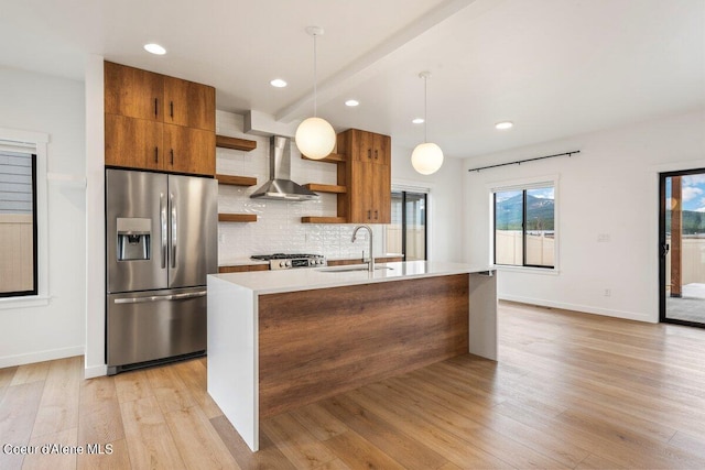 kitchen featuring stainless steel fridge, wall chimney exhaust hood, sink, light hardwood / wood-style flooring, and hanging light fixtures